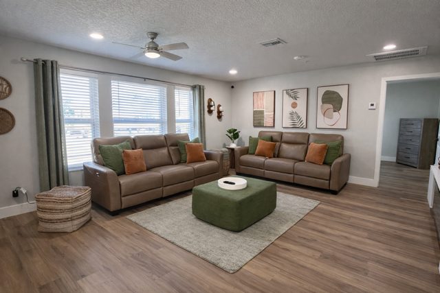 Sitting room with two sofas, a green ottoman and a ceiling fan at a Serenity Living home